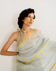 Woman wearing a light gray saree with yellow patterns against a white background