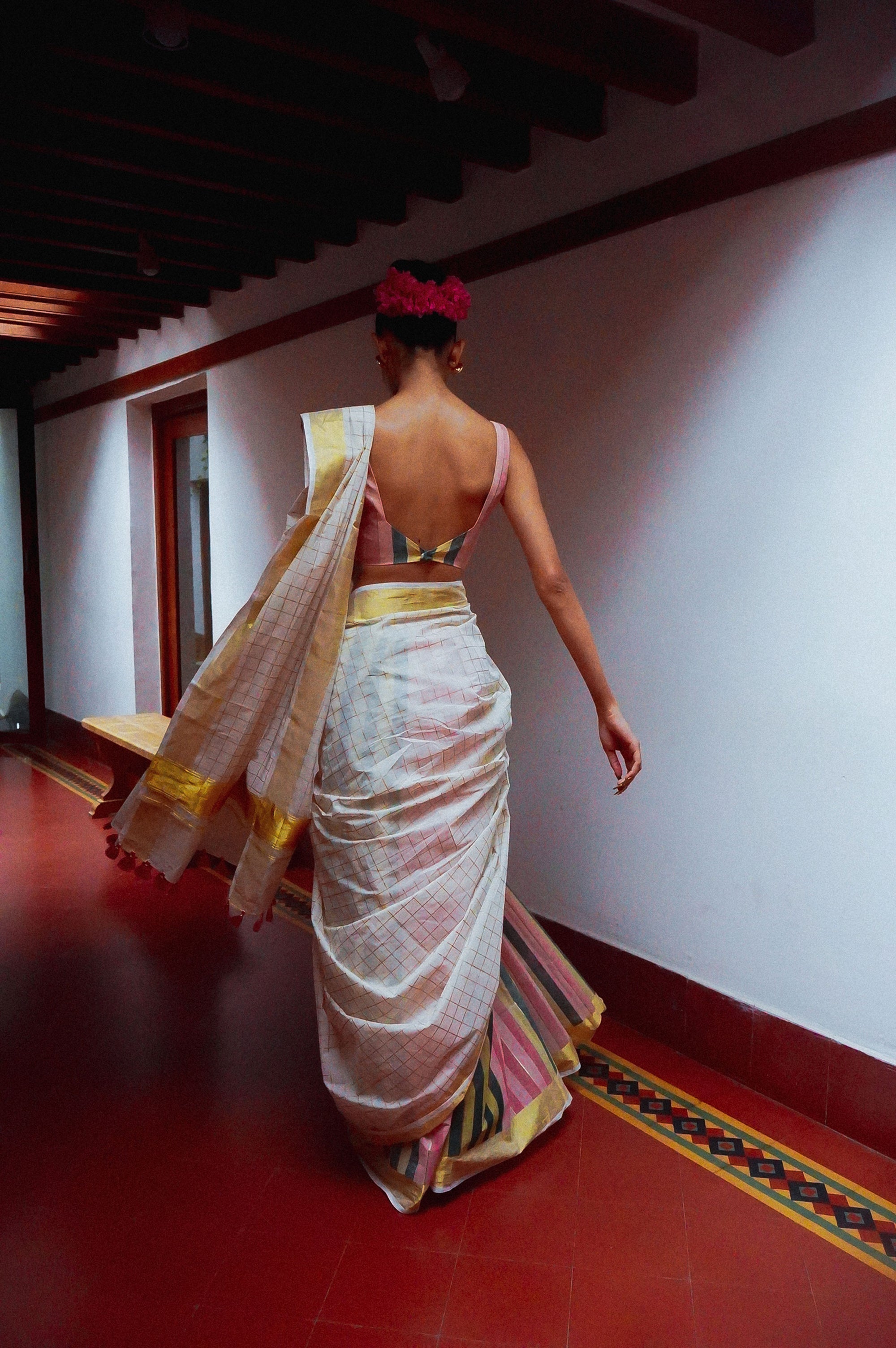 Woman in onam saree walking in a room with red flooring and white walls.