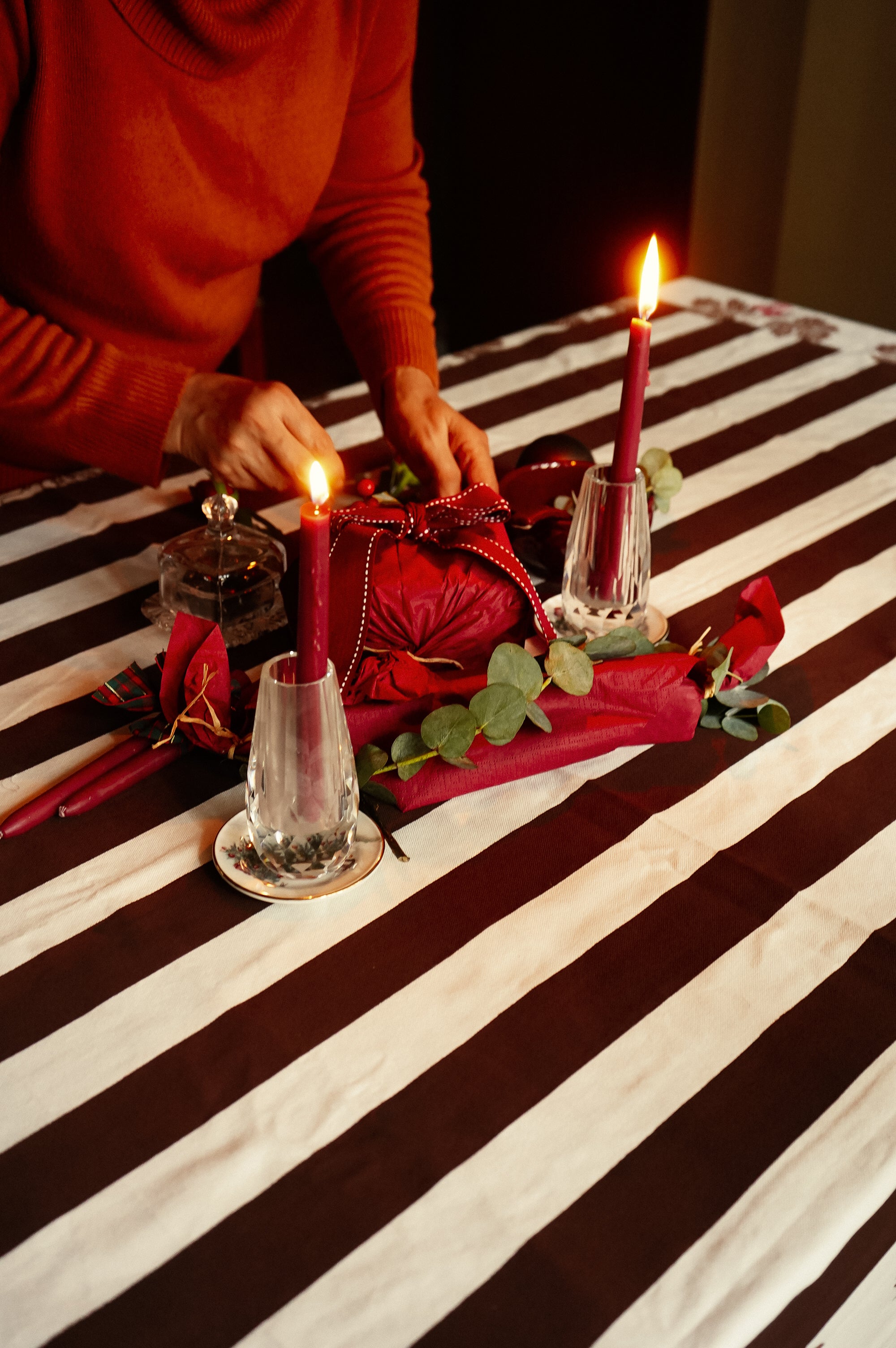 Person lighting candles on a table with red and white striped tablecloth for christmas