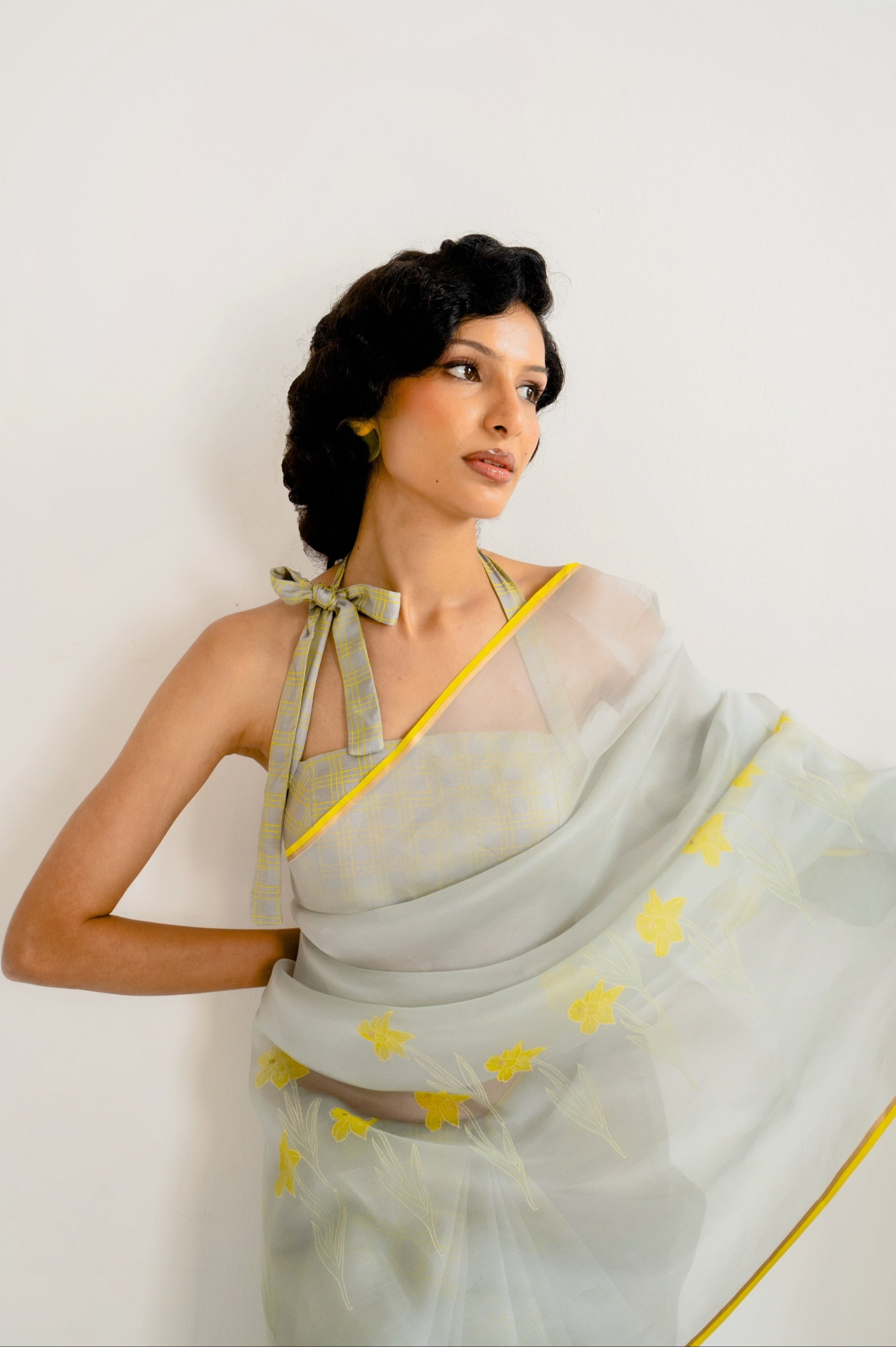 Woman wearing a light gray saree with yellow patterns against a white background